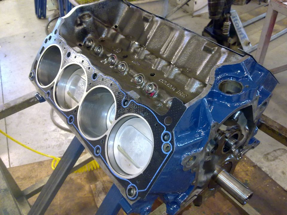 Blue painted engine block with pistons visible, on a stand