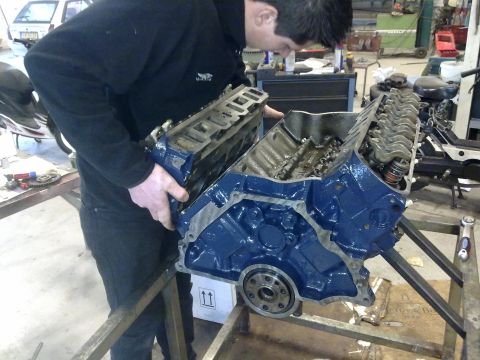 1984 Ford Bronco - A mechanic works on an engine block, disassembling or preparing it for reassembly.