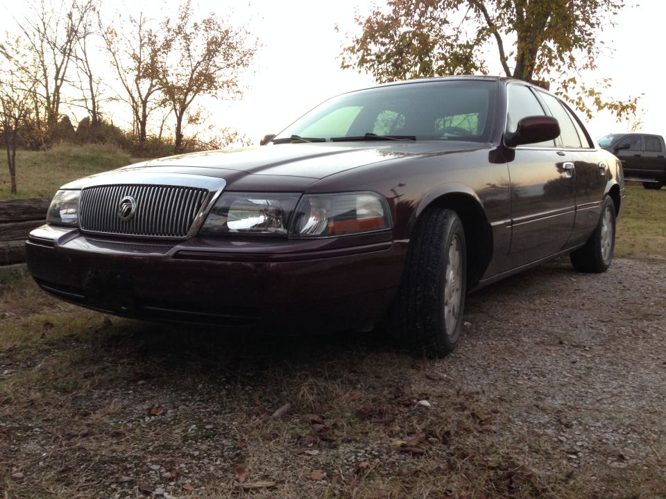 Maroon 2003 Mercury Grand Marquis parked outside with trees and another vehicle in the background