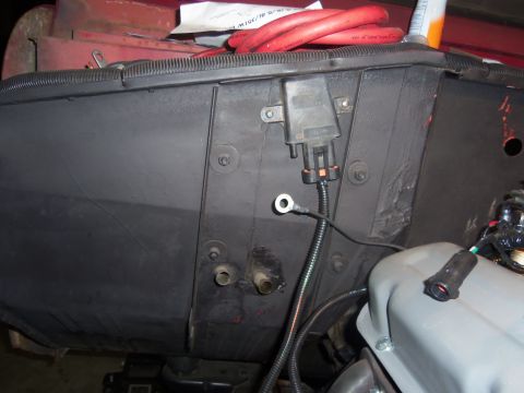 1968 Ford Bronco - Close-up view of engine bay wiring and a black plastic component with a connector, with red cables overhead.