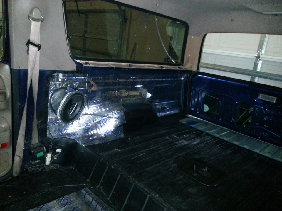 Interior view of a vehicle showing sound deadening material on the rear panel and a speaker installed