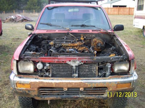 1991 Toyota Pickup/SR5 - Front view of a red 1991 Toyota Pickup with its hood open, revealing a damaged engine compartment and rusty front bumper.