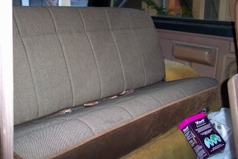 1986 Ford Bronco - The interior of a vehicle shows a bench seat with seatbelts and a box on the floor.