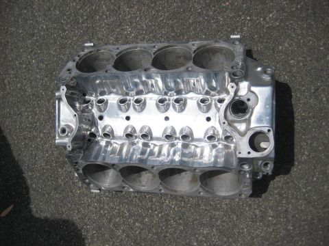 1972 Ford Ranchero - A polished aluminum V8 engine block rests on a dark asphalt surface, showing its internal cylinder bores and intake manifold bolt holes.