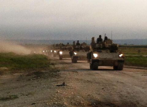 1982 Ford Bronco - A convoy of military vehicles drives down a dusty road as the sun sets.