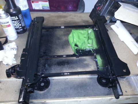 1994 Ford Bronco - A black metal seat frame is shown on a workbench, partially covered with green tape.