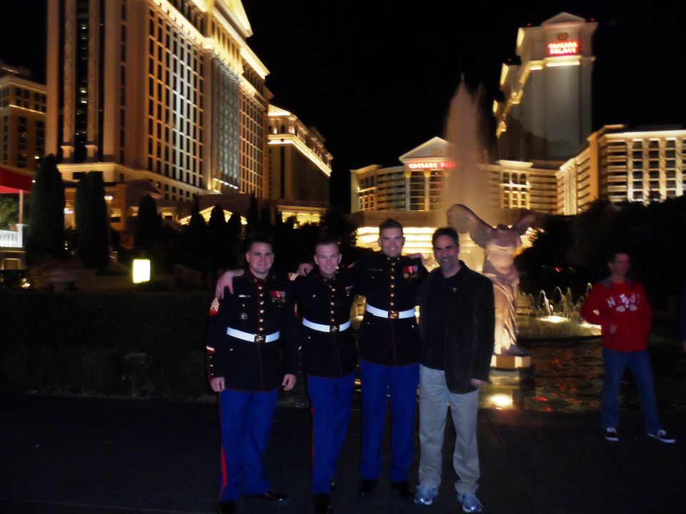 Four men posing at night in front of illuminated buildings and a fountain