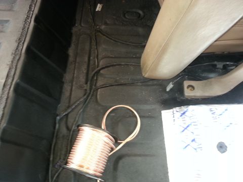1994 Ford Bronco - The interior floor of a vehicle shows wiring and a spool of copper wire next to a beige seat.