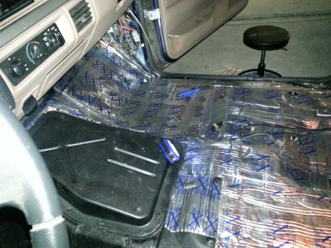 1994 Ford Bronco - The interior of a vehicle shows sound deadening material being applied to the floor, with parts of the dashboard and steering wheel visible.