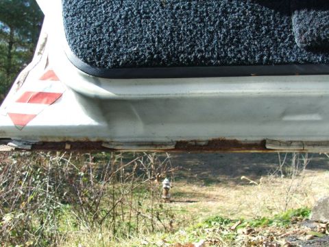 1988 Ford Crown Victoria LTD - The lower edge of a car door shows significant rust and wear, with black carpet visible above.