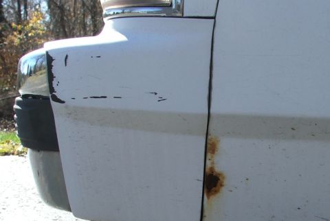 1988 Ford Crown Victoria LTD - Close-up of a white car's damaged fender and door, showing rust and chipped paint.