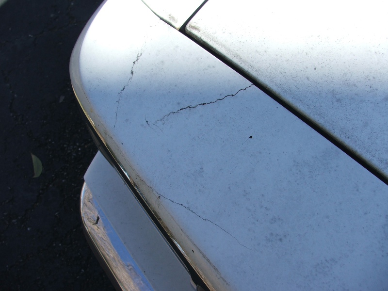 Close-up of cracked car hood and chrome bumper. Supermotors.net watermark visible