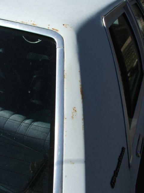 1988 Ford Crown Victoria LTD - Rust is visible on the white paint of a 1988 Ford Crown Victoria LTD, with a partial view of the quilted interior.