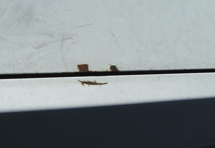 Rust spots on a white car panel, showing damage along a seam