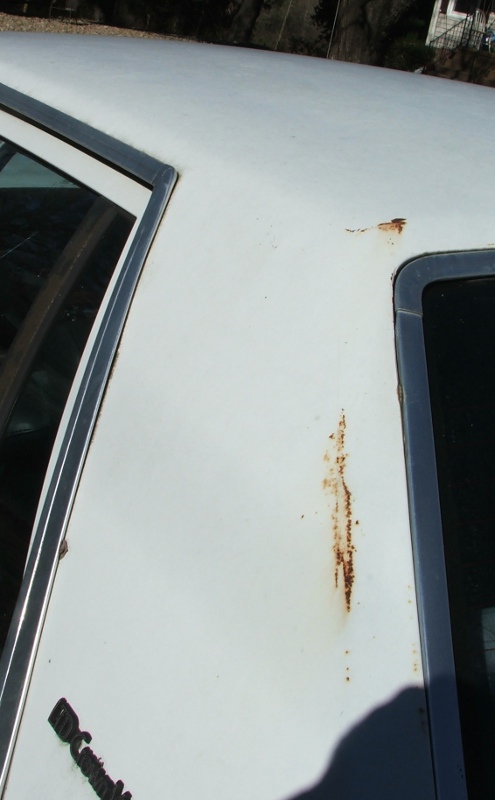 Close-up of white car roof with rust streaks and chrome trim around window frame