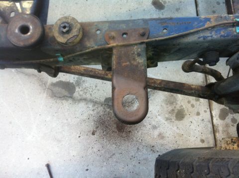 1979 Ford Bronco - Close-up of a heavily rusted vehicle frame, showing suspension components and a tow hook.