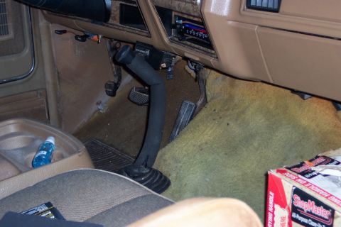 1986 Ford Bronco - The interior of a vehicle shows a floor shifter and pedals, with tan carpeting and dashboard.