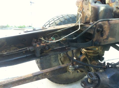 1979 Ford Bronco - Close-up view of the undercarriage of a heavily rusted vehicle, showing brake lines and suspension components.