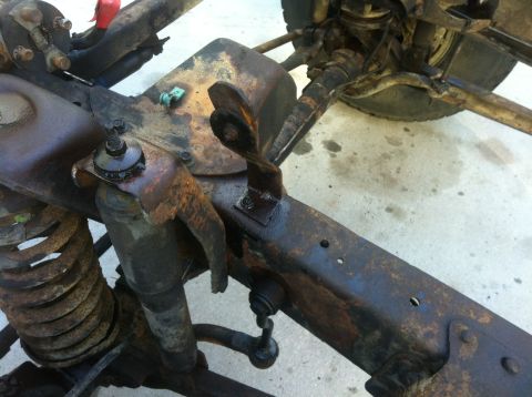 1979 Ford Bronco - Close-up view of heavily rusted vehicle frame and suspension components, including a shock absorber and coil spring.