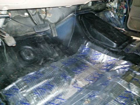1994 Ford Bronco - The floor of a vehicle is covered in sound deadening material, revealing exposed wiring and pedals.