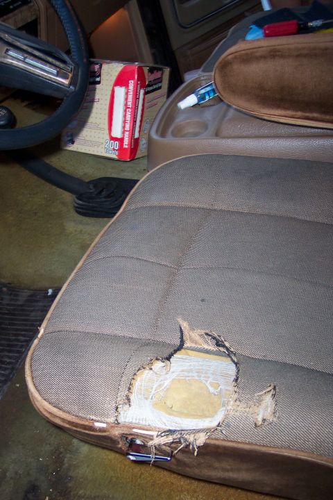 1986 Ford Bronco - Interior view of a vehicle showing a damaged seat and some items on the console.
