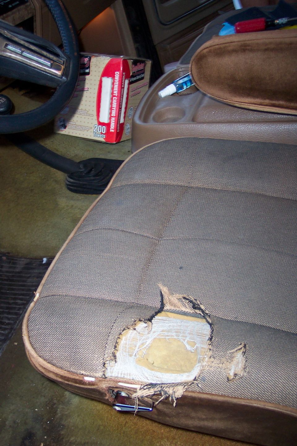 Torn tan cloth bucket seat interior showing exposed foam padding in vehicle cab
