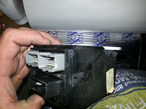 1994 Ford Bronco - A hand holds a black plastic electrical connector housing with multiple grey and white plugs, part of a vehicle's interior.