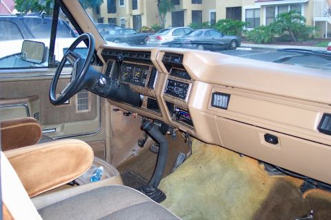 1986 Ford Bronco - The interior of an older truck shows the dashboard, steering wheel, and seats, with a water bottle on the floor.