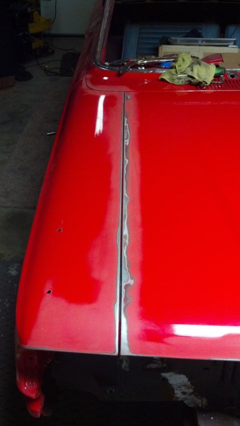 1964 Ford Fairlane - The seam between two body panels on a red car is being prepared for repair, showing exposed metal.