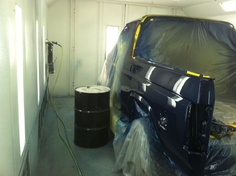 1982 Ford Bronco - A vehicle is being prepped for painting inside a booth with bright lights and a barrel nearby.