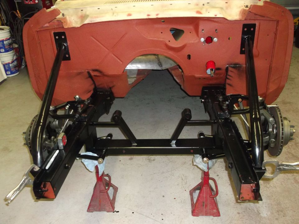 Car chassis on jack stands, showing front suspension and subframe. Red primer on firewall