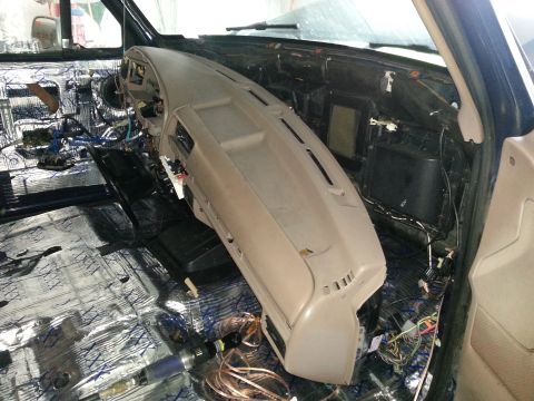 1994 Ford Bronco - The interior of a vehicle is shown with the dashboard disassembled, revealing wiring and sound dampening materials.