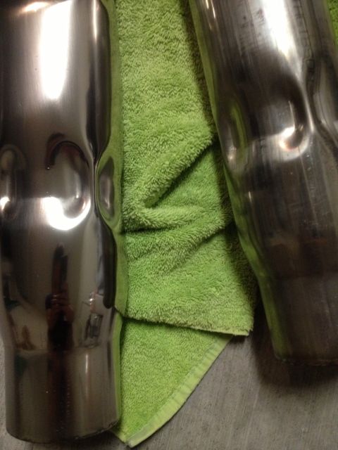 2013 Ford Mustang - Two exhaust pipes with visible dents, one polished and one showing wear, laid on a green towel.