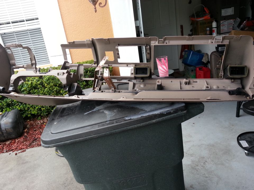 Tan dashboard assembly removed from a vehicle, resting on a trash bin