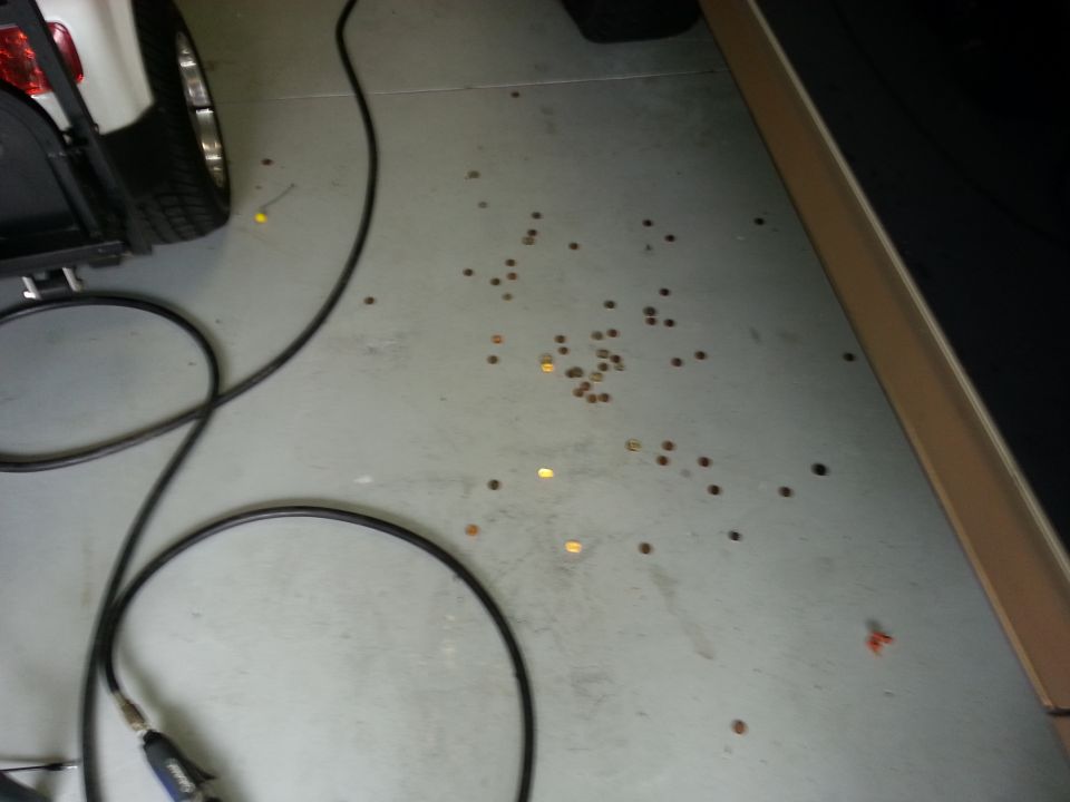 Scattered coins on a concrete garage floor with a black cable and part of a white vehicle visible