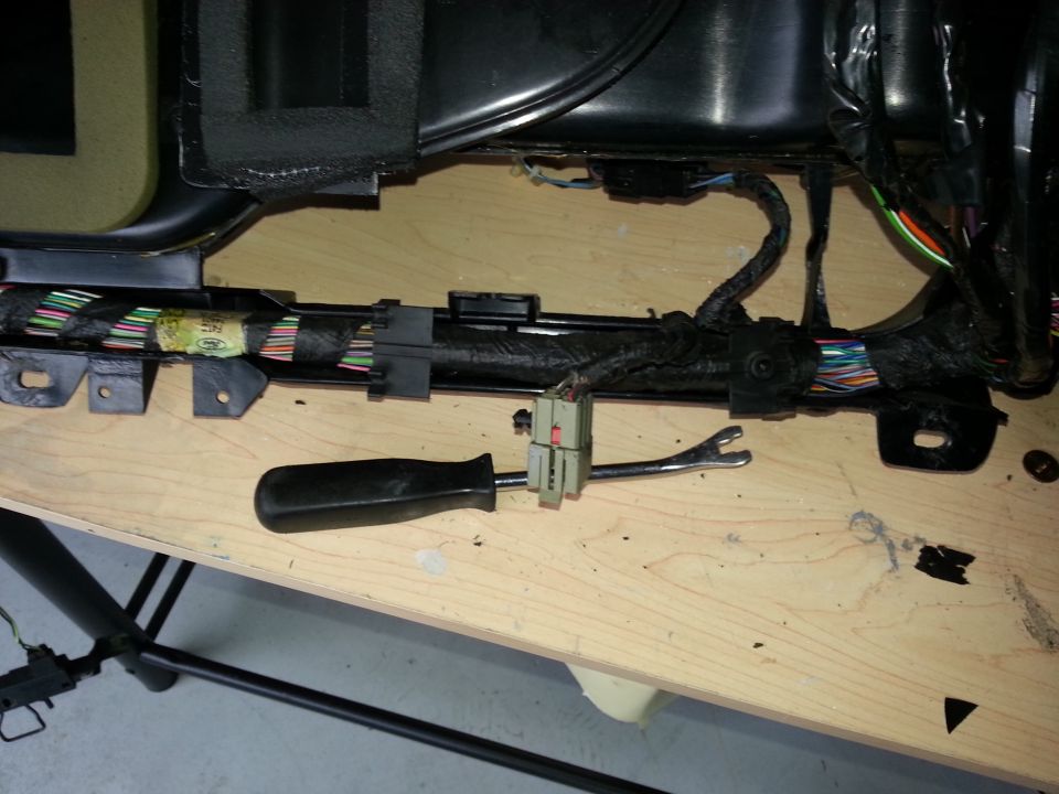 Vehicle wiring harness with tools on a wooden surface. A screwdriver and a wiring tool are visible