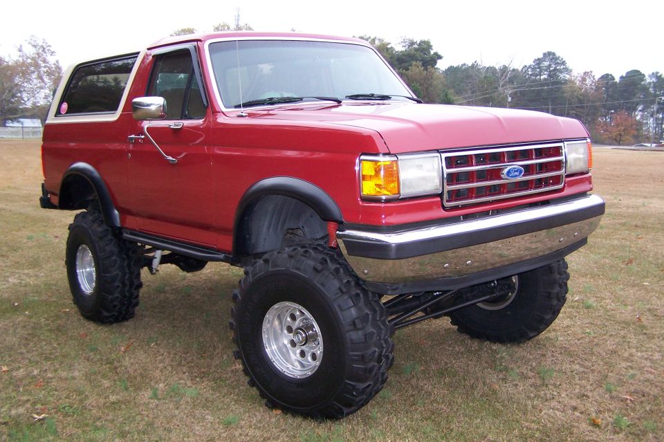 Red lifted 1990 Ford Bronco with chrome grille and large tires