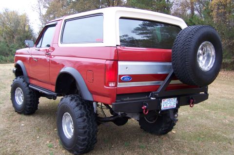 1990 Ford Bronco - This lifted Ford Bronco is shown from a rear 3/4 angle, equipped with large off-road tires and a spare tire carrier.