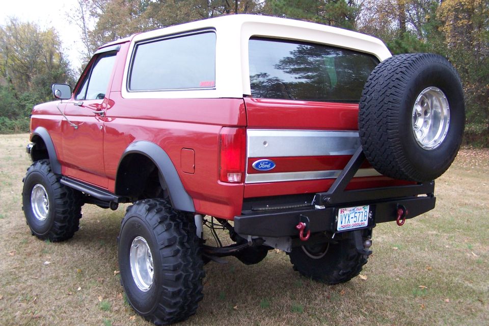 Red Ford Bronco with a tan roof, lifted suspension, and a spare tire mounted on the rear bumper