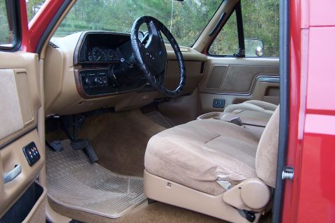 1990 Ford Bronco - The tan interior of a red truck shows the dashboard, steering wheel, and seats.
