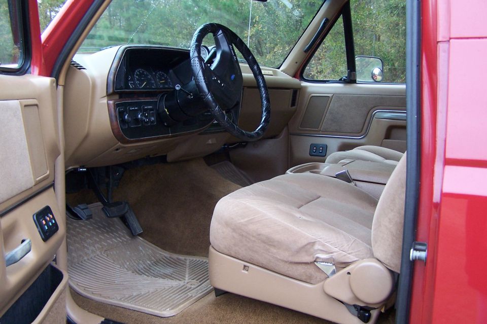 Interior view of a red truck's dashboard, steering wheel, and tan seats