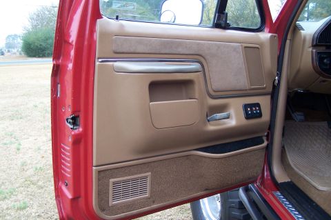 1990 Ford Bronco - Interior view of a red 1990 Ford Bronco, focusing on the driver's side door panel with tan upholstery and speaker grille.