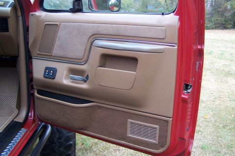 1990 Ford Bronco - The interior door panel of a red Ford Bronco shows tan trim and power window controls.
