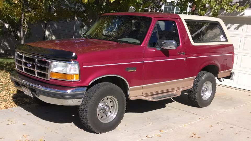 Red 1995 Ford Bronco with tan lower body trim and a white removable top, parked in a driveway