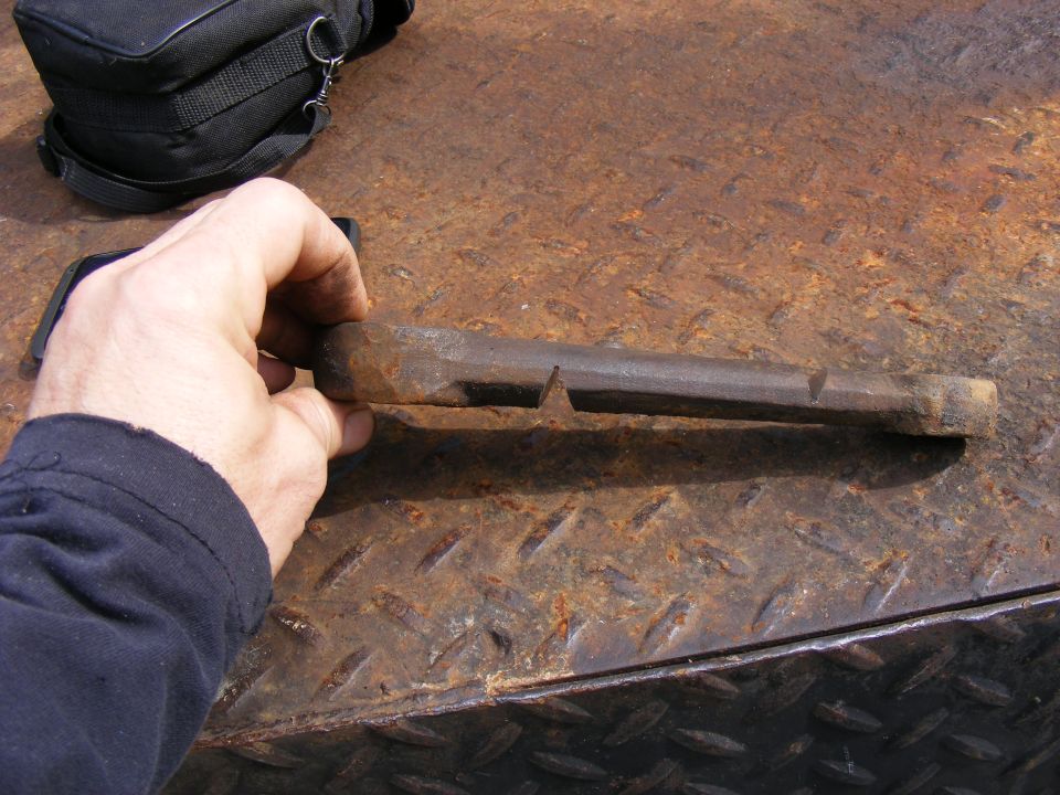 Hand holding a rusty metal tool over a rusty metal surface.