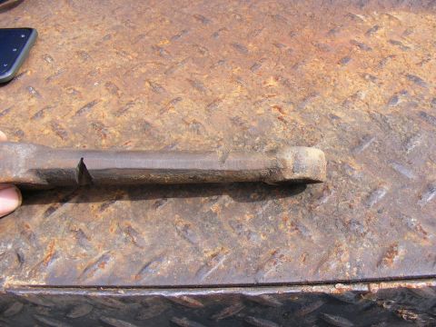 Close-up of a rusty metal bar with a notch on a diamond plate surface.