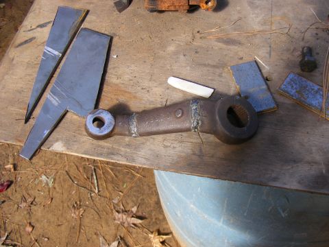 Metal steering linkage part with '30' stamped on it, on a wooden surface with metal scraps.