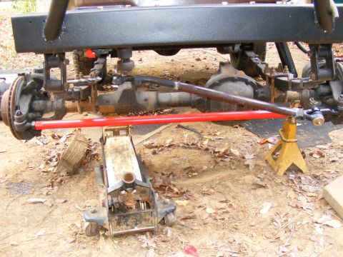 Red tie rod installed on front axle of vehicle, supported by jack and jack stand.