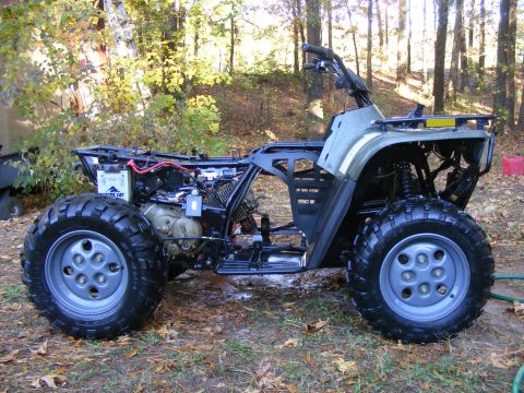 Arctic Cat ATV with engine exposed, parked outside in a wooded area
