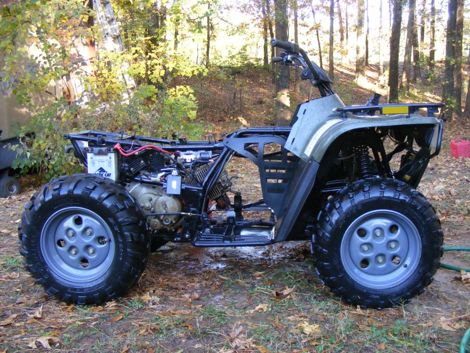 Arctic Cat ATV with engine exposed, parked outside in a wooded area